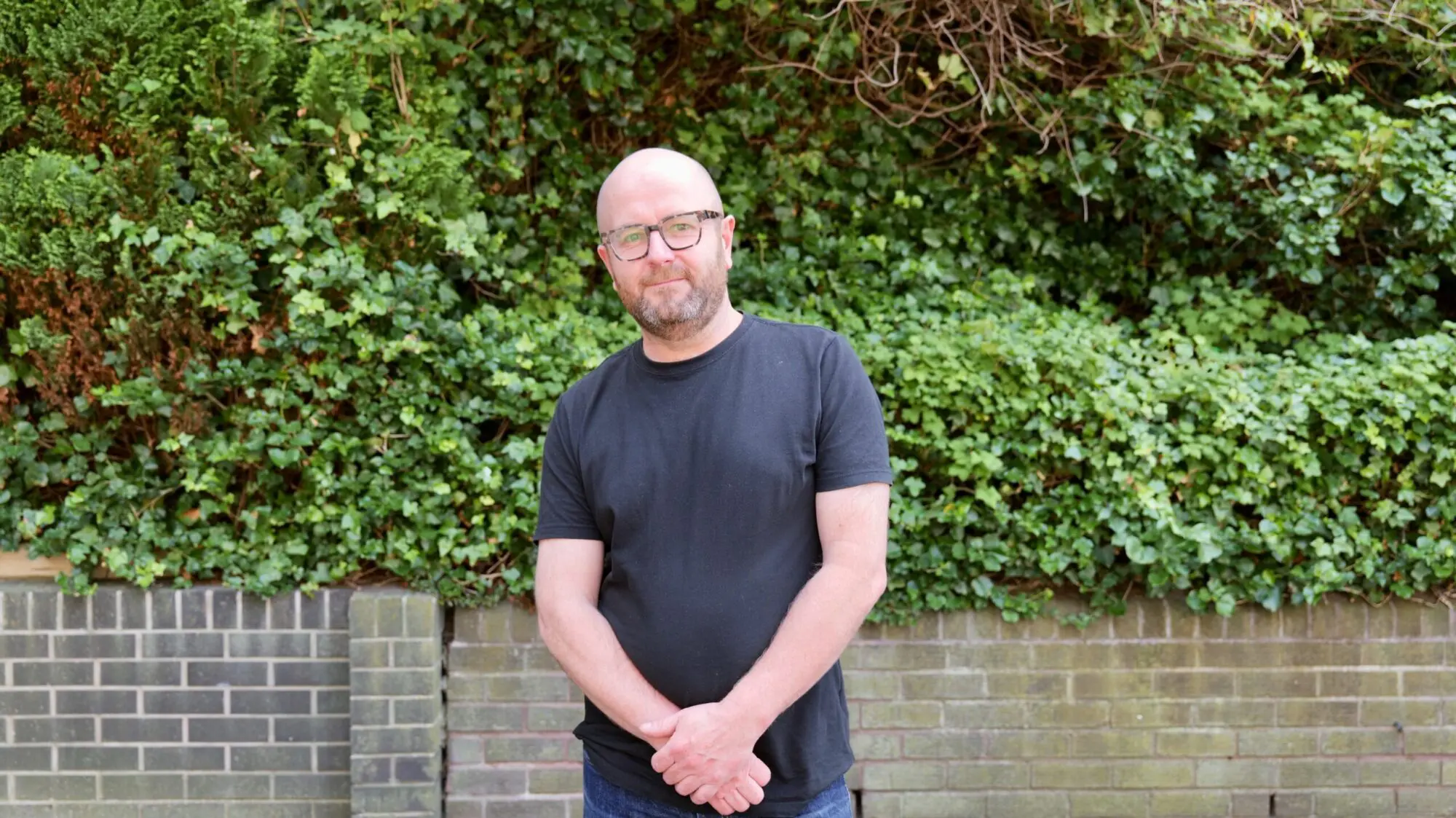 Founder of lintels.in, Jamie Noble, stands in front of wall and foliage at Meadowbank House